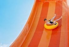 Child sitting on a yellow ring, sliding down an orange water slide
