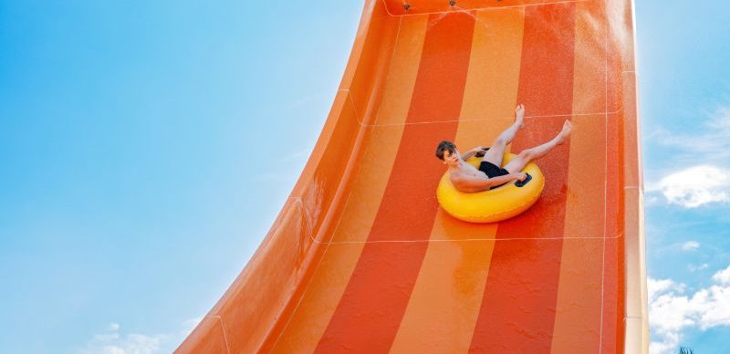 Child sitting on a yellow ring, sliding down an orange water slide